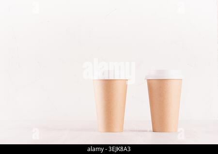Coffee packing mockup -  two kraft brown paper cups with white cap on white wood board with copy space, coffee shop interior. Mo Stock Photo
