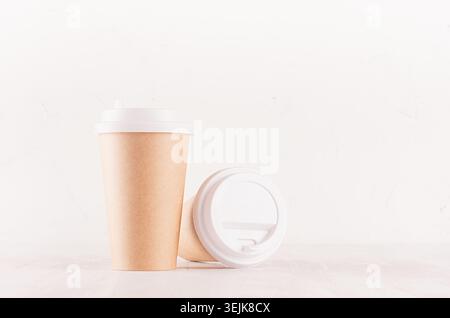 Coffee packing mockup -  kraft brown paper cups and blank white cap on white wood board with copy space, coffee shop interior. M Stock Photo