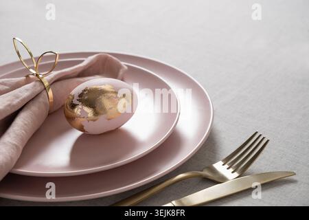Elegant Easter table setting with golden egg on pink plate Stock Photo