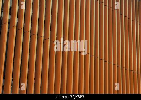 Close-up of a modern building facade featuring vertical orange architectural slats. Geometric pattern and exterior design background. Stock Photo