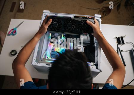 High-angle view of computer technician carefully inserting high-performance graphic card inside gaming desktop, upgrading powerful system with vibrant Stock Photo