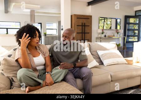 African American couple sitting on beige sectional sofa, woman gesturing while man touching knee Stock Photo