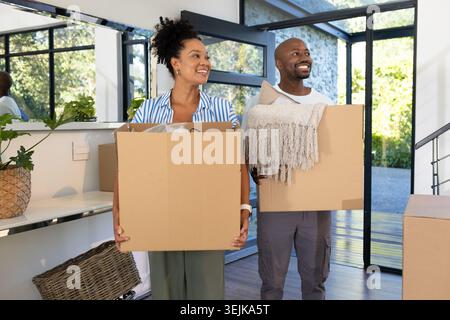 African American couple carrying cardboard boxes and holding fringed throw in bright entryway Stock Photo