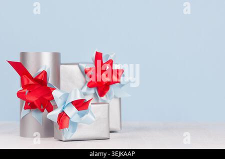 Bright metallic paper gift boxes with red and blue satin ribbons and bows on soft light white wood board. Stock Photo