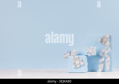 Christmas festive background - soft light blue gift boxes with shiny silver ribbons and bows on white wood board. Stock Photo