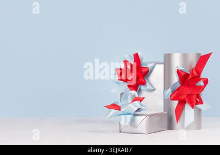 Elegance festive silver gift boxes with red and blue ribbons, bows closeup on white wood table, blue wall, copy space. Stock Photo