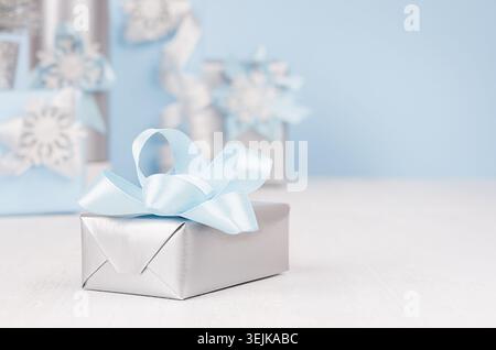 Festive silver metallic gift box with blue silk bow closeup and different elegance soft christmas presents on background in blur Stock Photo