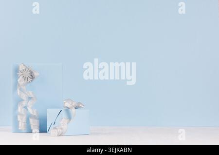 Two blue pastel paper gift boxes with shiny silver ribbons and bows on soft light white wood board. Stock Photo
