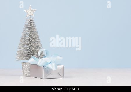 Gentle home decor for New Year celebration - silver gift boxes and small sparkles fir on white wood table and  soft light blue w Stock Photo