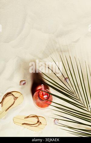 Summertime tropical vacation on sea beach background - cold fruit pink drink, slippers, seashells, green palm leaf on sand in su Stock Photo