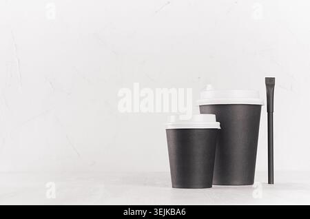 Coffee mockup - big and small black paper cups with white caps and sugar bag on white wood table with copy space, coffee shop in Stock Photo