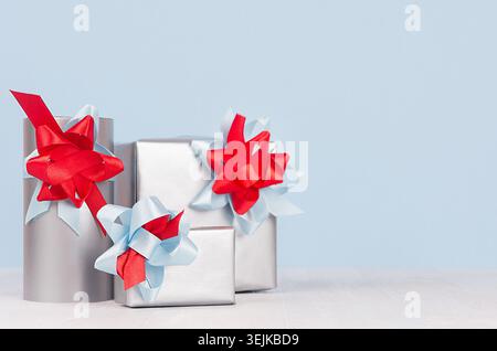 Christmas festive background - silver gift boxes with red and blue ribbons and bows on white wood board. Stock Photo