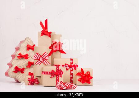 Christmas preparing - gift wrapping boxes of kraft with red ribbons and bows and christmas tree on white wood table. Stock Photo