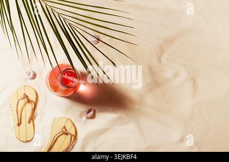 Rest and relax on summer tropical beach picnic - green palm leaf, cold pink drink in glass bottle, slippers, seashells in sunlig Stock Photo