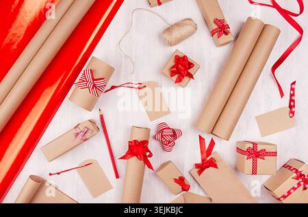 Christmas preparations background - wrapping paper, gift boxes, red ribbon and bows, twine as festive pattern on white wooden bo Stock Photo