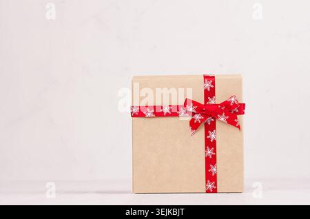 Elegance festive a gift box of kraft paper with a red ribbon and bow on white wood board with copy space. Stock Photo