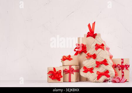 Christmas festive composition of different gift boxes with red ribbons and bows around christmas tree on white wood background. Stock Photo