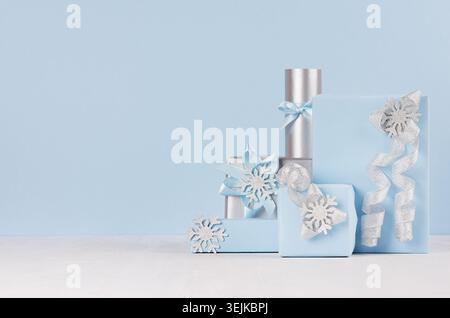 Christmas festive background - soft light blue gift boxes with shiny silver ribbons and bows on white wood board. Stock Photo