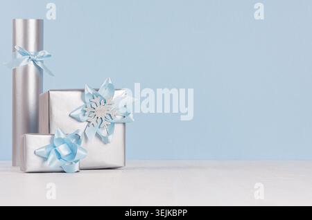 Three silver metallic gift boxes with shiny ribbons and bows on soft light white wood board and pastel blue wall. Stock Photo
