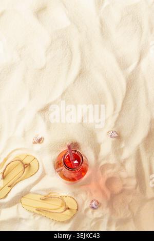 Tropical picnic and recreation on sandy beach - fresh cold fruit pink cocktail in glass bottle, slippers, seashells on sand, bor Stock Photo