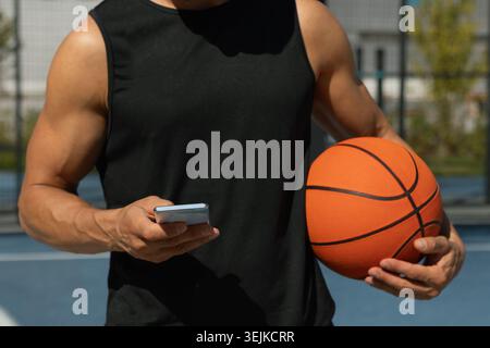 Basketball player or sports caucasian man using smartphone after outdoor training. Outdoors game. Relax, game interval. Stock Photo