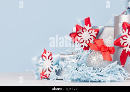 Christmas background - silver glittering ball with red silk bow closeup, blur and decorations on soft light blue color backdrop. Stock Photo