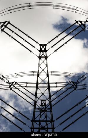 Power pole, cables and insulators of a high-voltage line viewed from below with blue white sky background Stock Photo