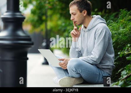 Remote worker or freelancer focused on work solution look on laptop sitting in urban park outdoors Stock Photo