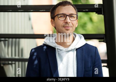 Casual business man millennial in eyeglasses and casual hoodie and blazer outside office building Stock Photo