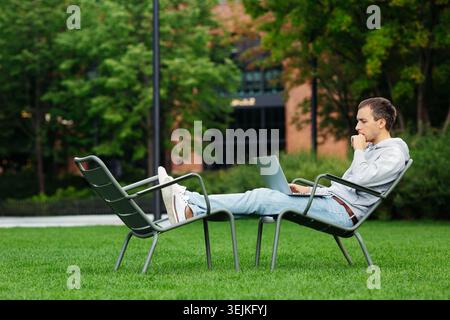 Pensive man entrepreneur work remote on laptop think on modern startup outdoors on backyard or park Stock Photo