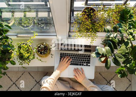 Woman writer use laptop at home sitting on floor at windowsill. Work remotely on covid-19 lockdown Stock Photo
