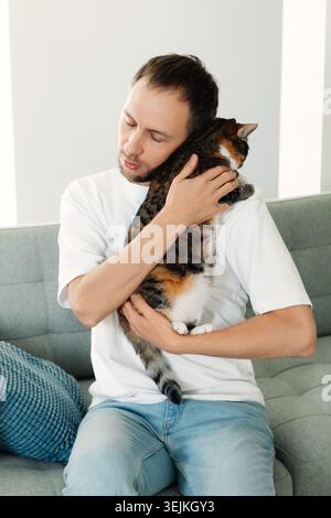 Depressed man hugging cat. Tired unhappy stressed male cuddling with pet sitting on couch at home Stock Photo