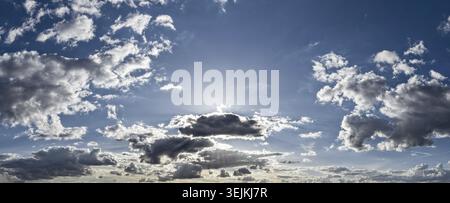 Panoramic photo of the dramatic, contrasting cloud sky with sunrays shining through the clouds behind the standing, obscured sun Stock Photo