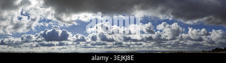 Panoramic photo of the dramatic, contrasting cloud sky with sunrays shining through the clouds behind the standing, obscured sun Stock Photo