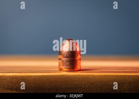 Macro close up of a brand new unfired 45 ACP pistol bullet component standing on a wooden table surface. Stock Photo