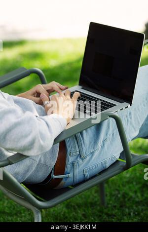 Close up arms of blogger man with laptop working outdoors in garden, sitting on chair. Rear view Stock Photo
