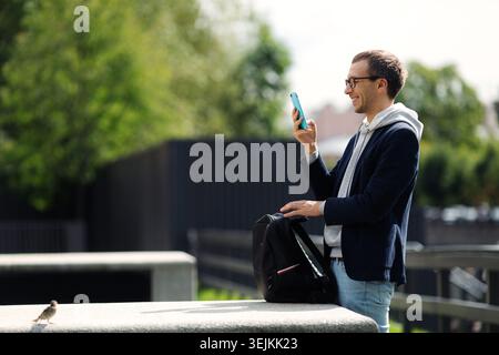 Excited casual man with backpack for laptop read text message in smartphone messenger app outdoors Stock Photo