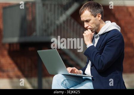 Focused casual businessman read email on laptop, network for project outdoors using 5g connection Stock Photo