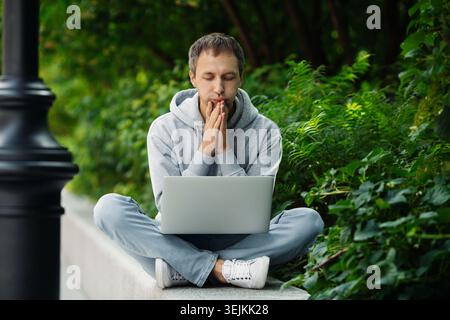 Pensive entrepreneur businessman look at laptop screen concerned working remotely from urban park Stock Photo