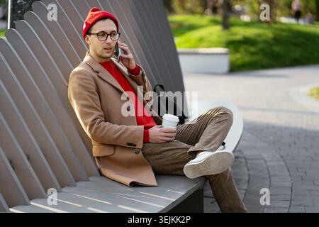Serious man on phone call sit with coffee on park bench. Freelance casual businessman use smartphone Stock Photo