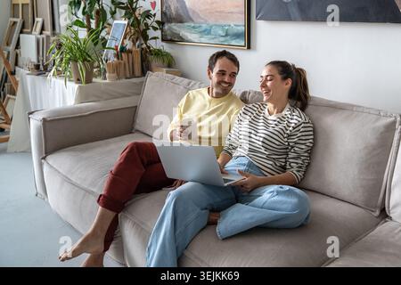Happy family married couple man and woman enjoying watching comedy movie on laptop together. Stock Photo