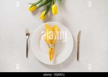 Easter table setting with yellow tulips, white plate, eggs and bunny. Stock Photo