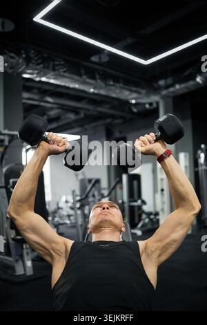 Strong man doing dumbbell bench press in gym Stock Photo