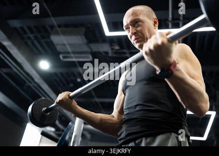 Strong athletic man doing barbell biceps curl in modern gym Stock Photo