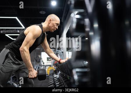 Strong athletic man doing one arm dumbbell row workout in modern gym Stock Photo