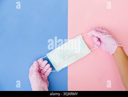 Hands in gloves keep medical mask on pink background. copy space Stock Photo