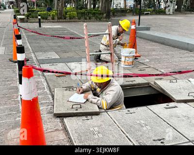 Utility workers inspect underground infrastructure during maintenance work on a sidewalk in Mexico City, Mexico Stock Photo