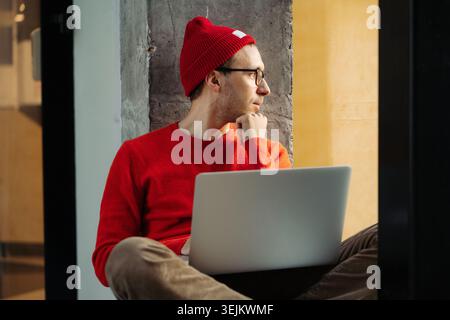 Focused freelancer designer, writer with laptop sit pensive on windowsill think on new project idea Stock Photo