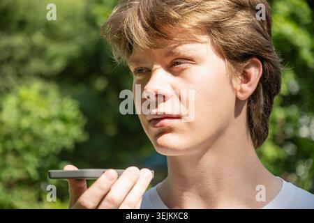 Young man recording voice message and using virtual voice assistant by phone Stock Photo