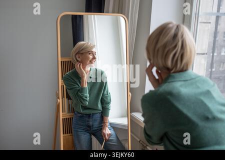 Joyful smiling woman appreciating own reflection in mirror, looking with positivity and confidence. Stock Photo